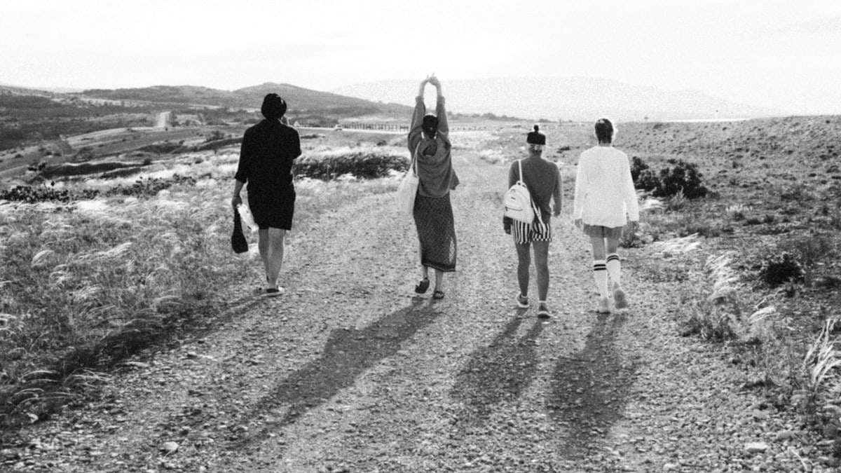 grayscale photo of 4 women walking on the road